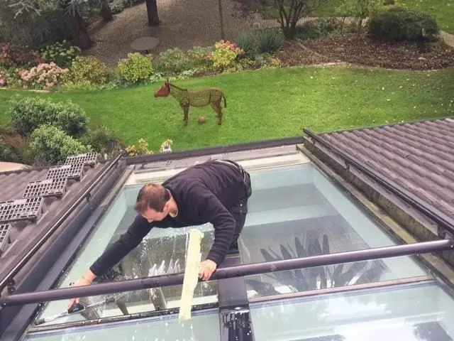 Mitarbeiter reinigt ein Glasdach im Garten kniend von außen.