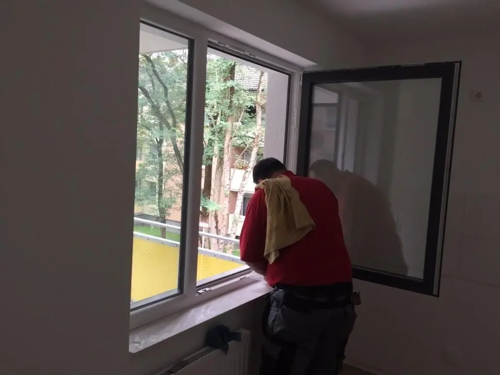 Mitarbeiter im roten Shirt reinigt einen Fensterrahmen von innen.