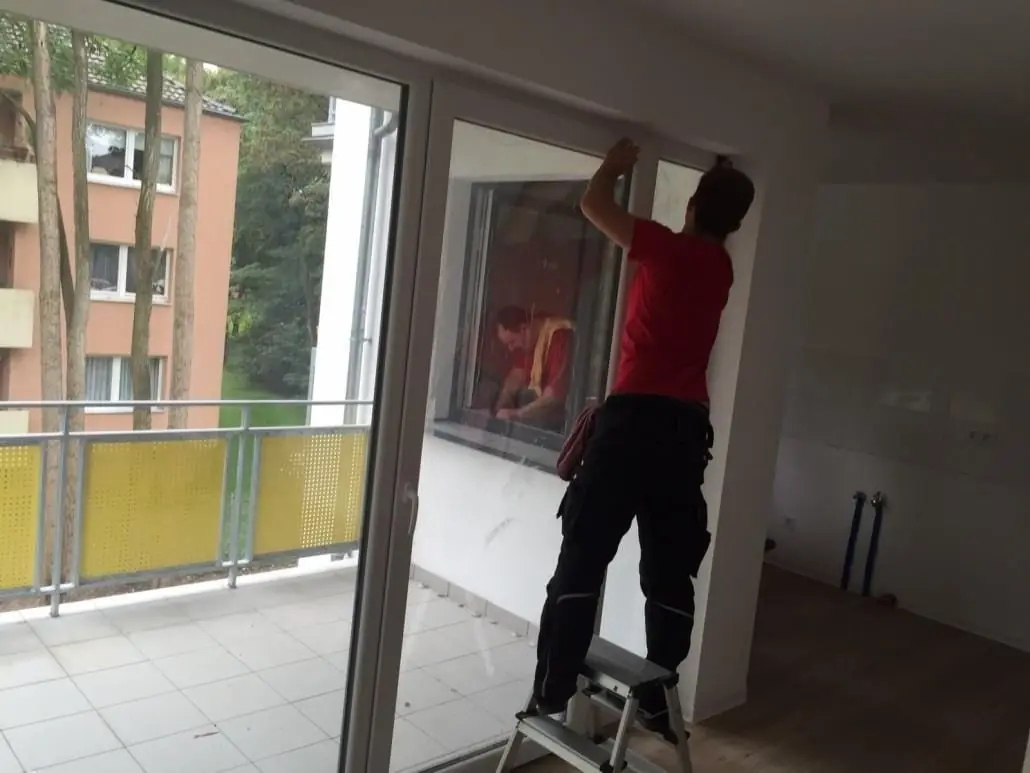 Mitarbeiter reinigt eine Balkontür von innen.
