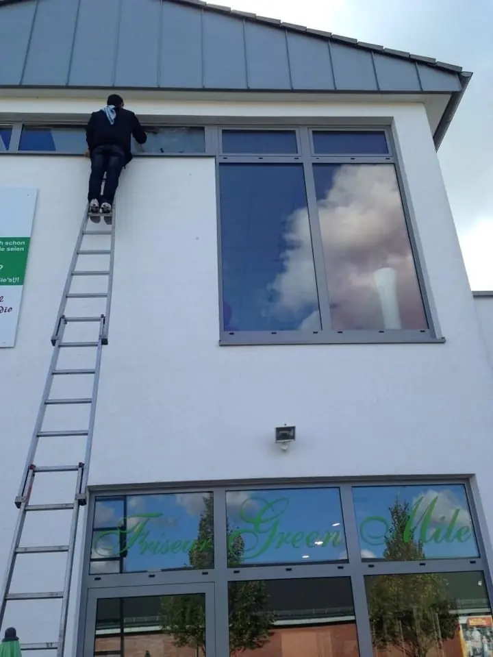 Glasreiniger auf einer Leiter an der Fassade eines Hauses.