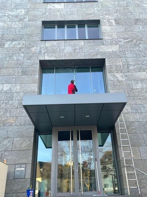 Eingangsbereich eines Bürohauses mit Steinfassade, darüber ein Glasreiniger an der verglasten Front.