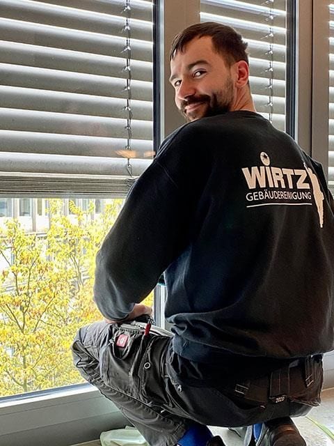 Lächelnder WIRTZ-Mitarbeiter kniet auf einer Fensterbank.