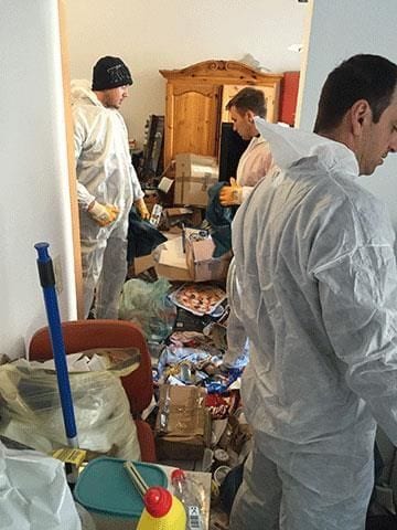 Mitarbeiter in Schutzanzügen räumen die vermüllte Wohnung.
